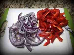 Red pepper and red onion cut into slices on a white cutting board